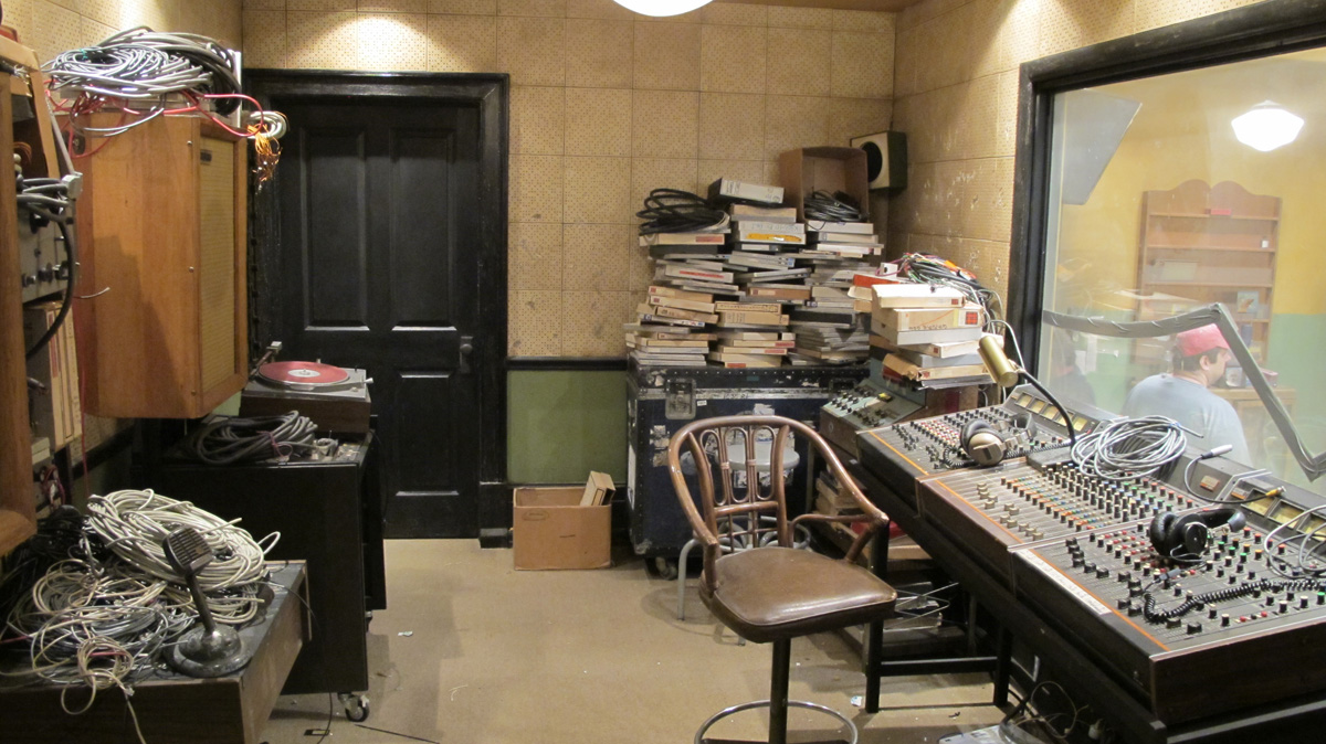 A cluttered production room with mixers and a black door