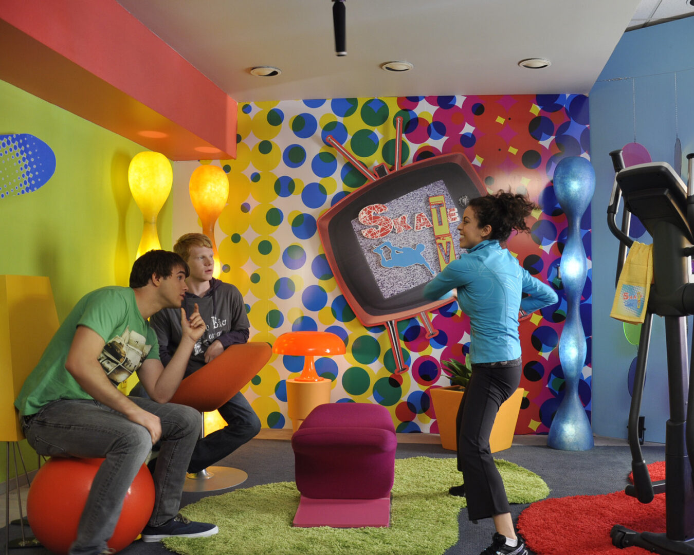 A dancing woman and two men in a colorful room